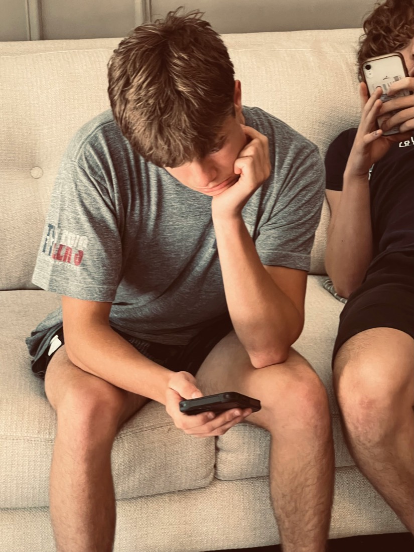 Two teenage boys on a couch, each absorbed in his own phone